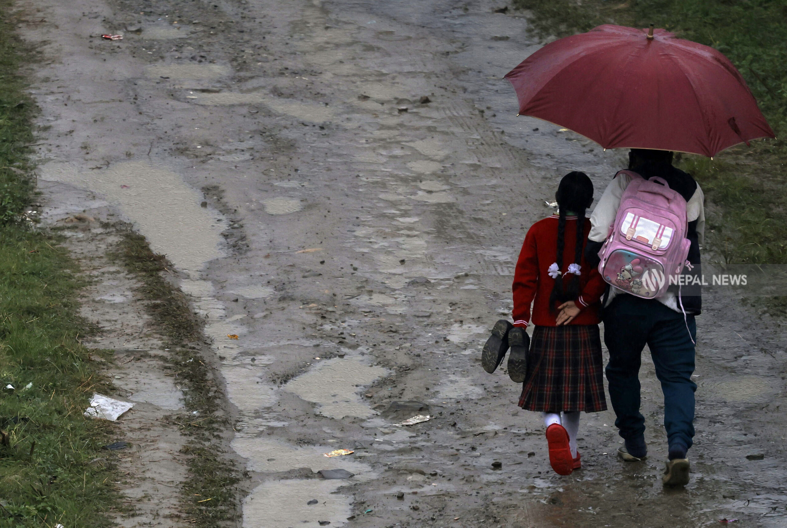 Girl walks to school with shoes in hand on muddy road